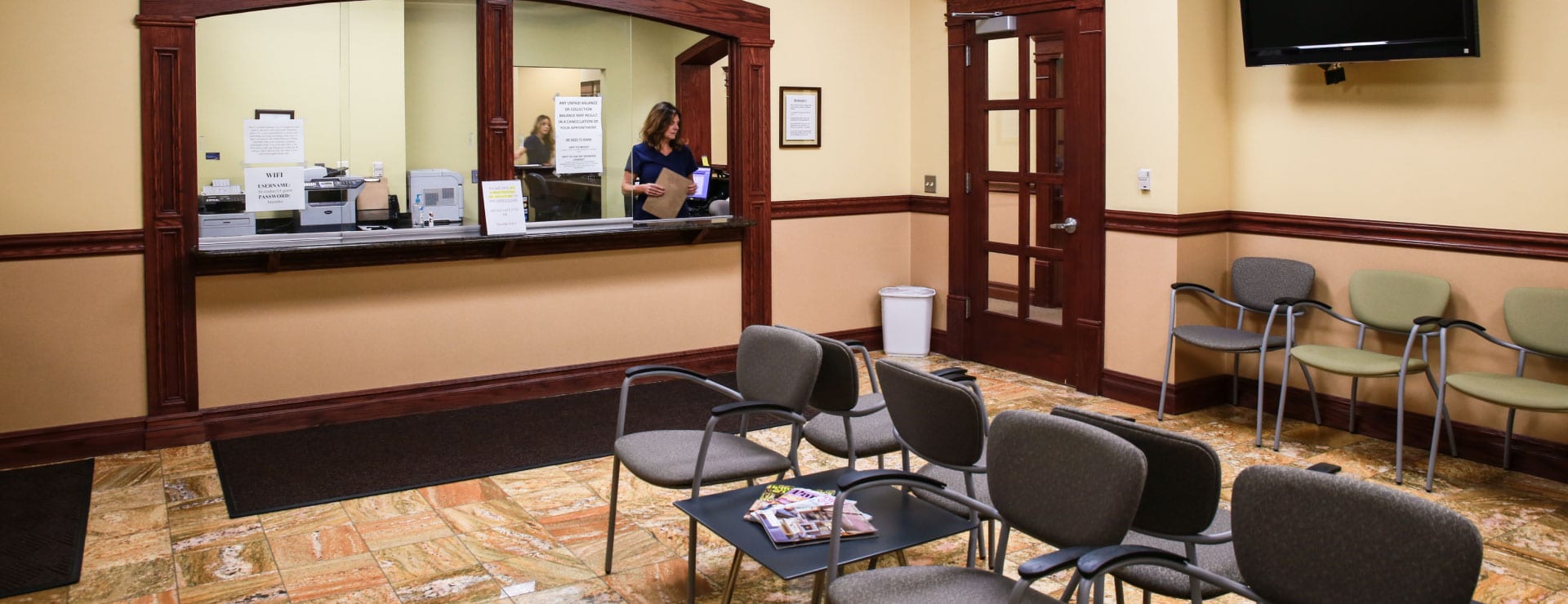 Clinic waiting room with rows of chairs and the reception window